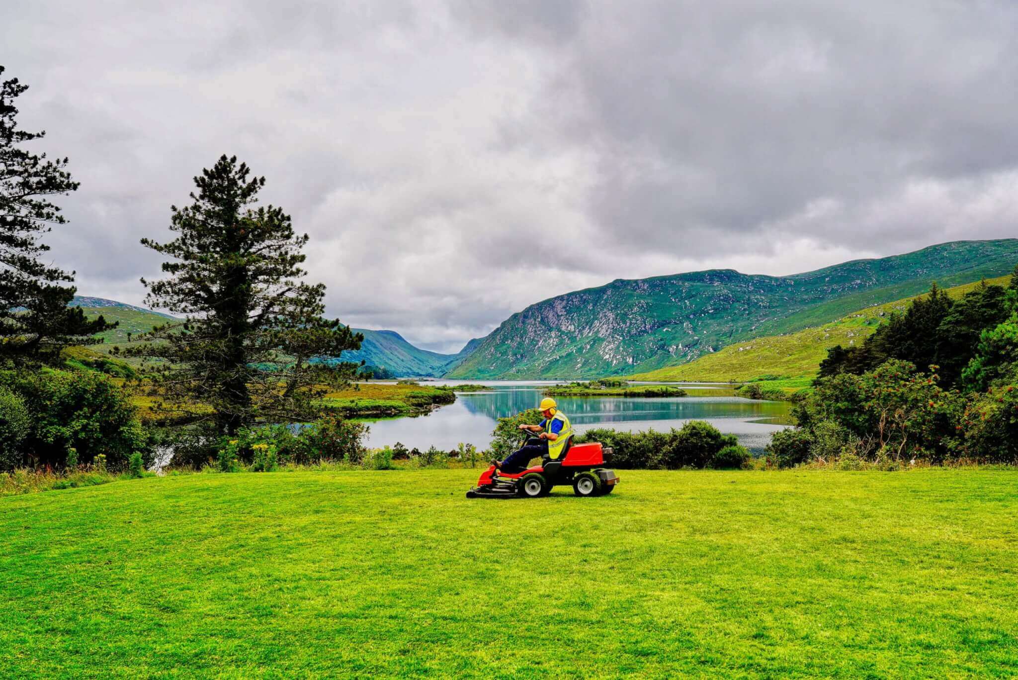 Un hombre montado en una cortadora de césped cerca de un lago en Irlanda, dedicado al paisajismo.